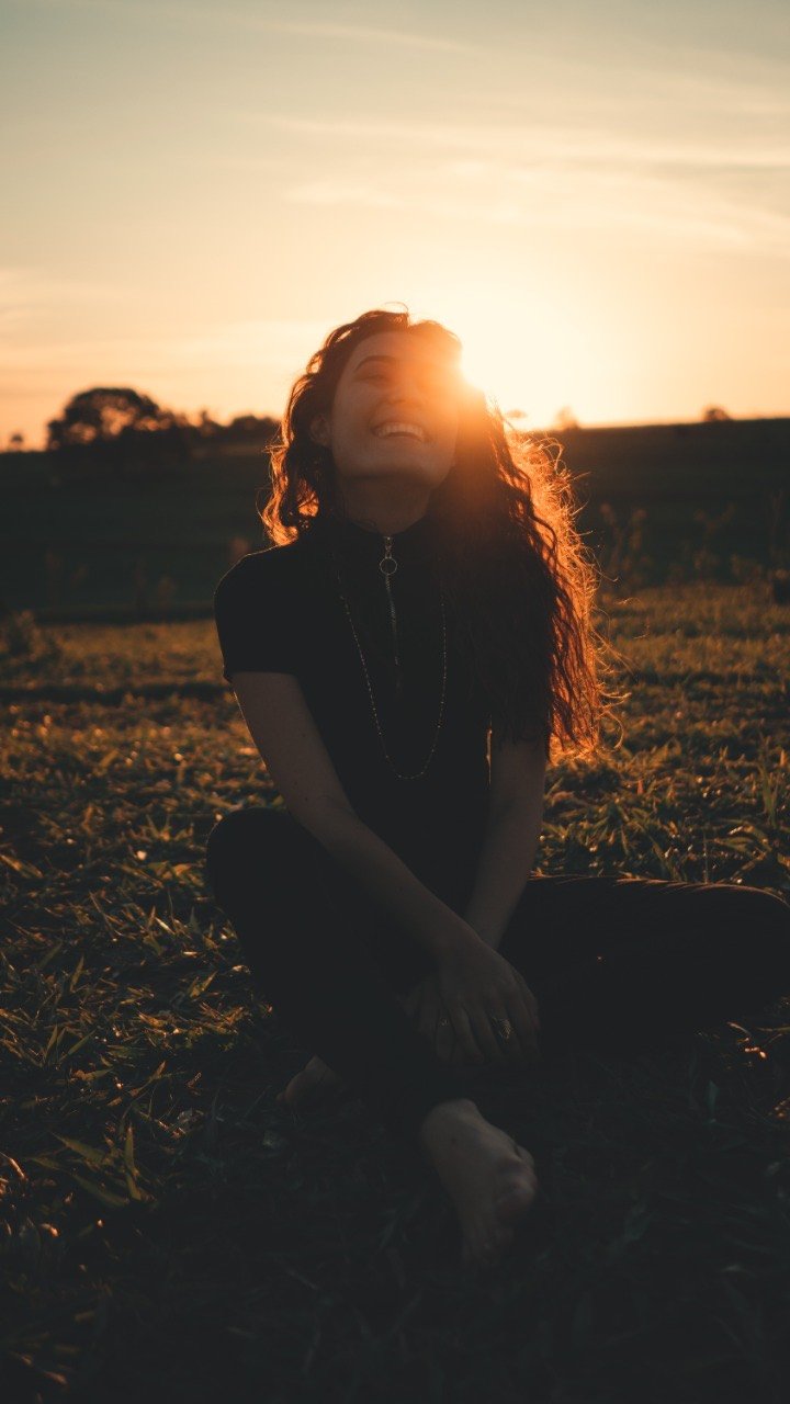Mulher sorrindo ao pôr do sol, sentada na grama