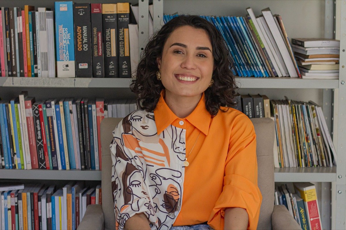 Jullìa Guimarães sorrindo em frente a uma estante de livros